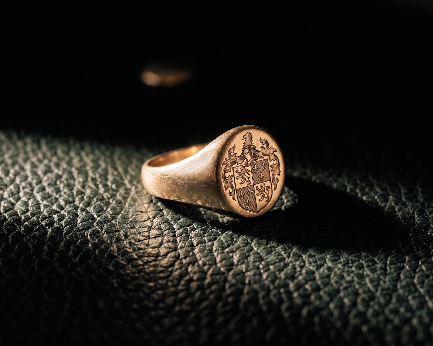A gold signet ring engraved with a family coat of arms, resting on dark green leather.